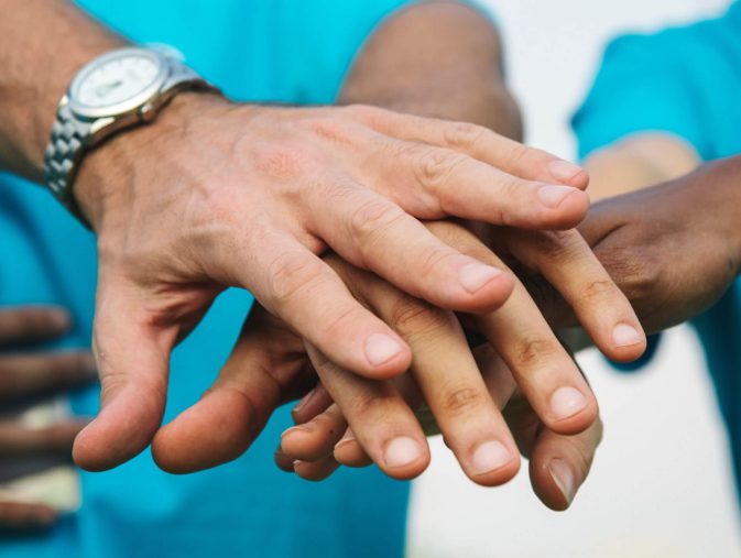Hände verschiedener Personen liegen übereinander, symbolisieren Gemeinschaft und Unterstützung.